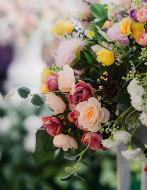 A vibrant floral arrangement featuring a mix of roses, carnations, and other blooms in shades of pink, yellow, and peach, accented with greenery and eucalyptus leaves. The flowers are arranged in a lu