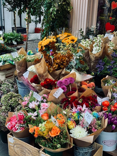 A variety of fresh flower bouquets arranged outdoors on display, wrapped in brown paper and tied with ribbons. The bouquets include colorful blooms such as pink lilies, orange roses, red carnations, p